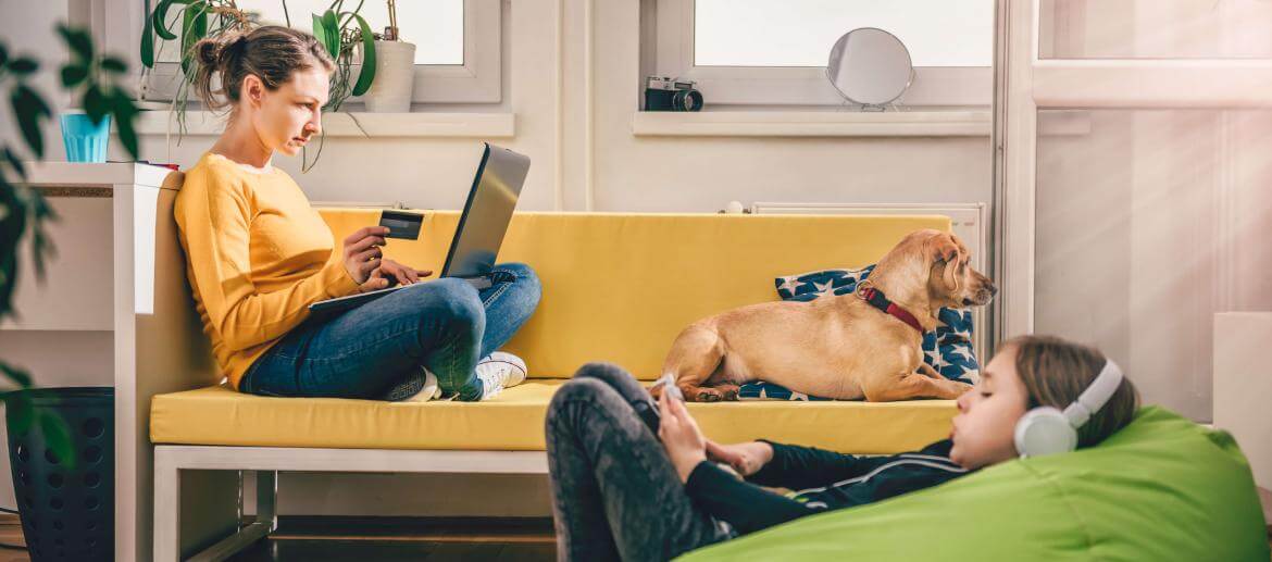 A photo of a woman doing her computer work, a dog sitting on the sofa and a girl listening music on headphones